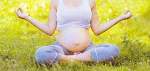 Pregnant woman yoga outdoors in summer day on the grass
